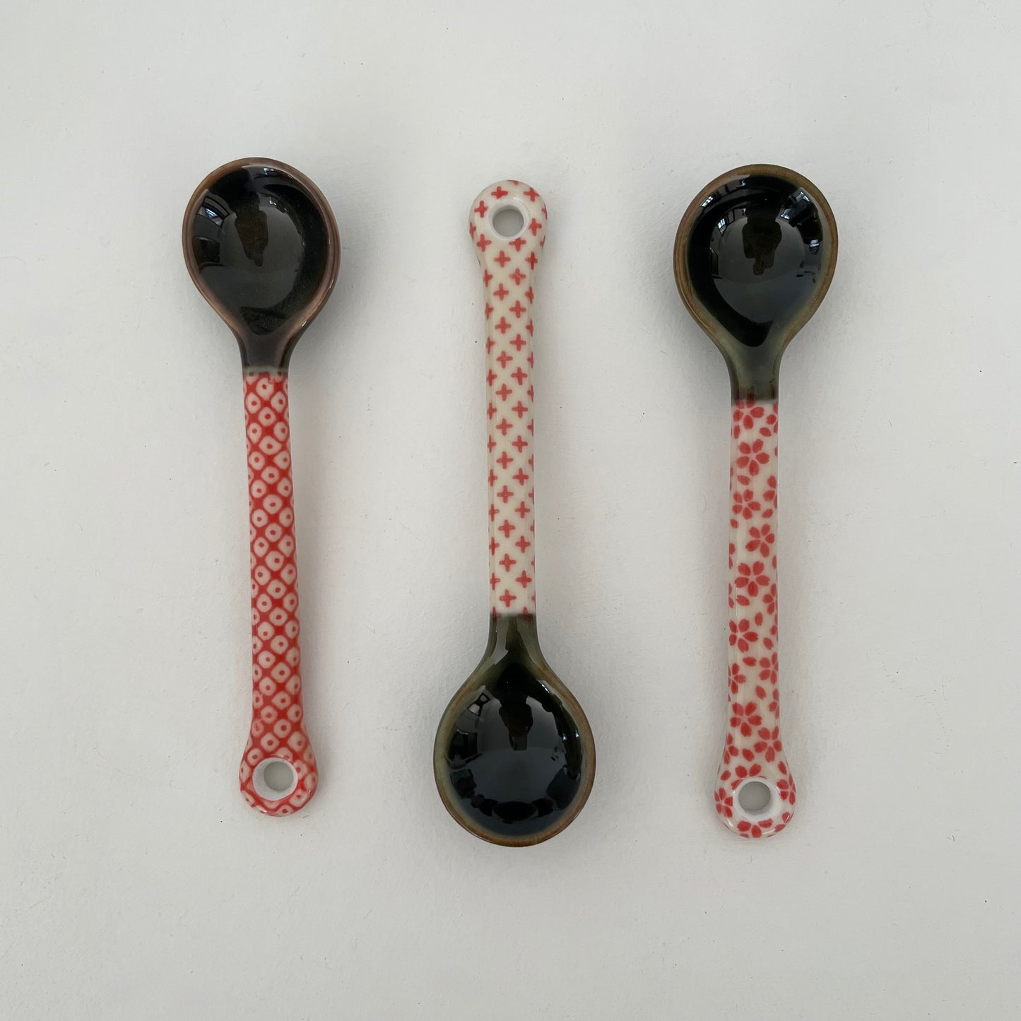 handmade small Japanese pottery spoon for coffee or tea in red and cream dot, cross, and flower patterns