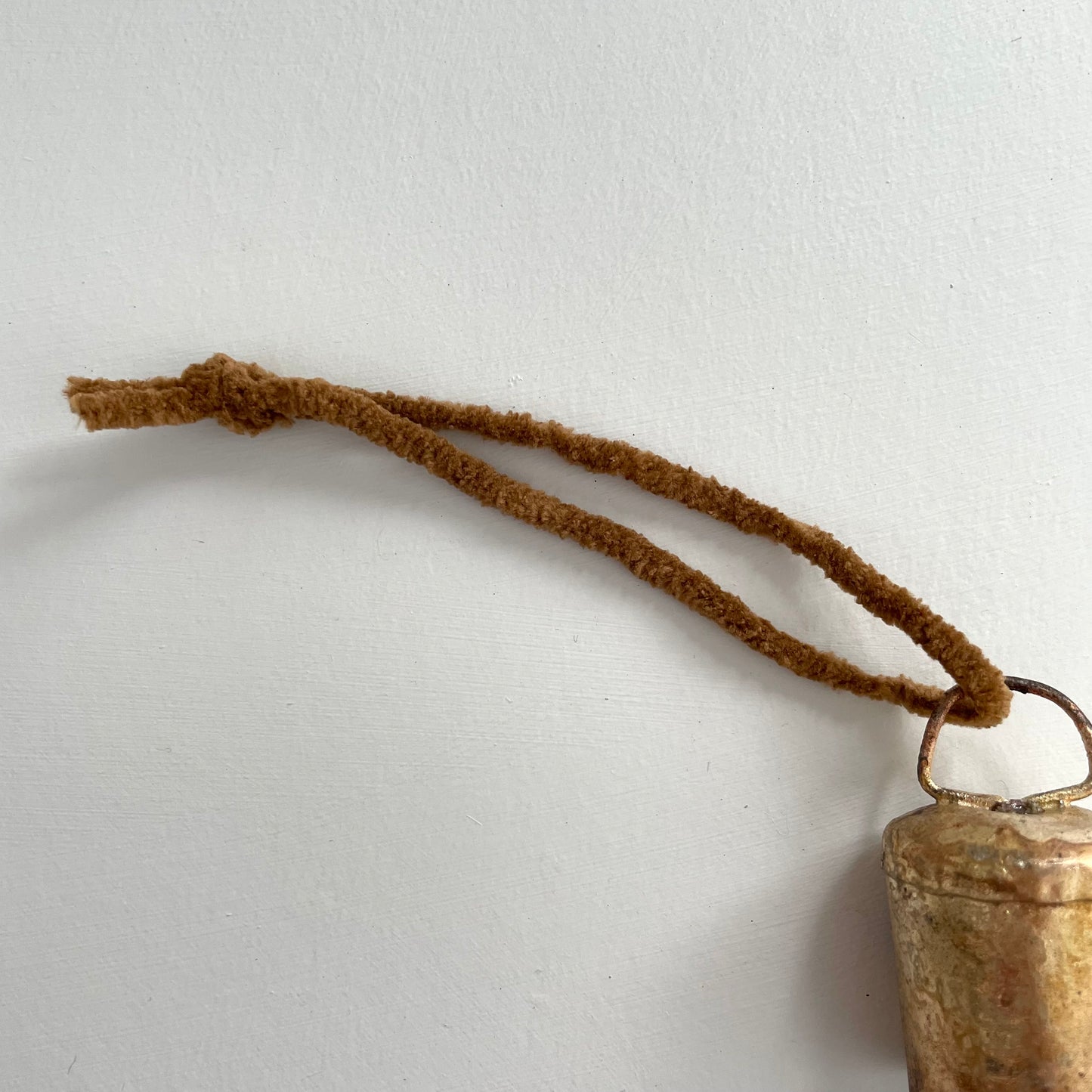 1 3/4 inch flat top tin bell with brass finish strung on twine suede and jute to make an ornament with cognac brown suede cord