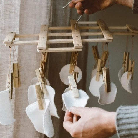 eco bamboo hanging laundry drying rack with clothespins holding reusable beauty rounds