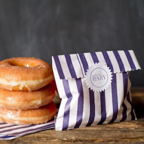 navy blue and white striped paper candy treat and gift party bags with white starburst label and a stack of donuts