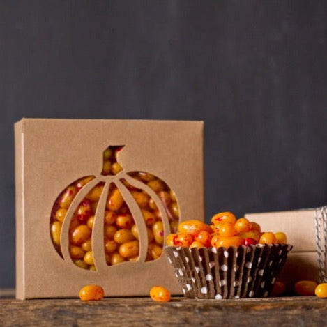 individual tan kraft cardboard cookie boxes with pumpkin cutout window next to a brown and white polka dot cupcake liner filled with candy