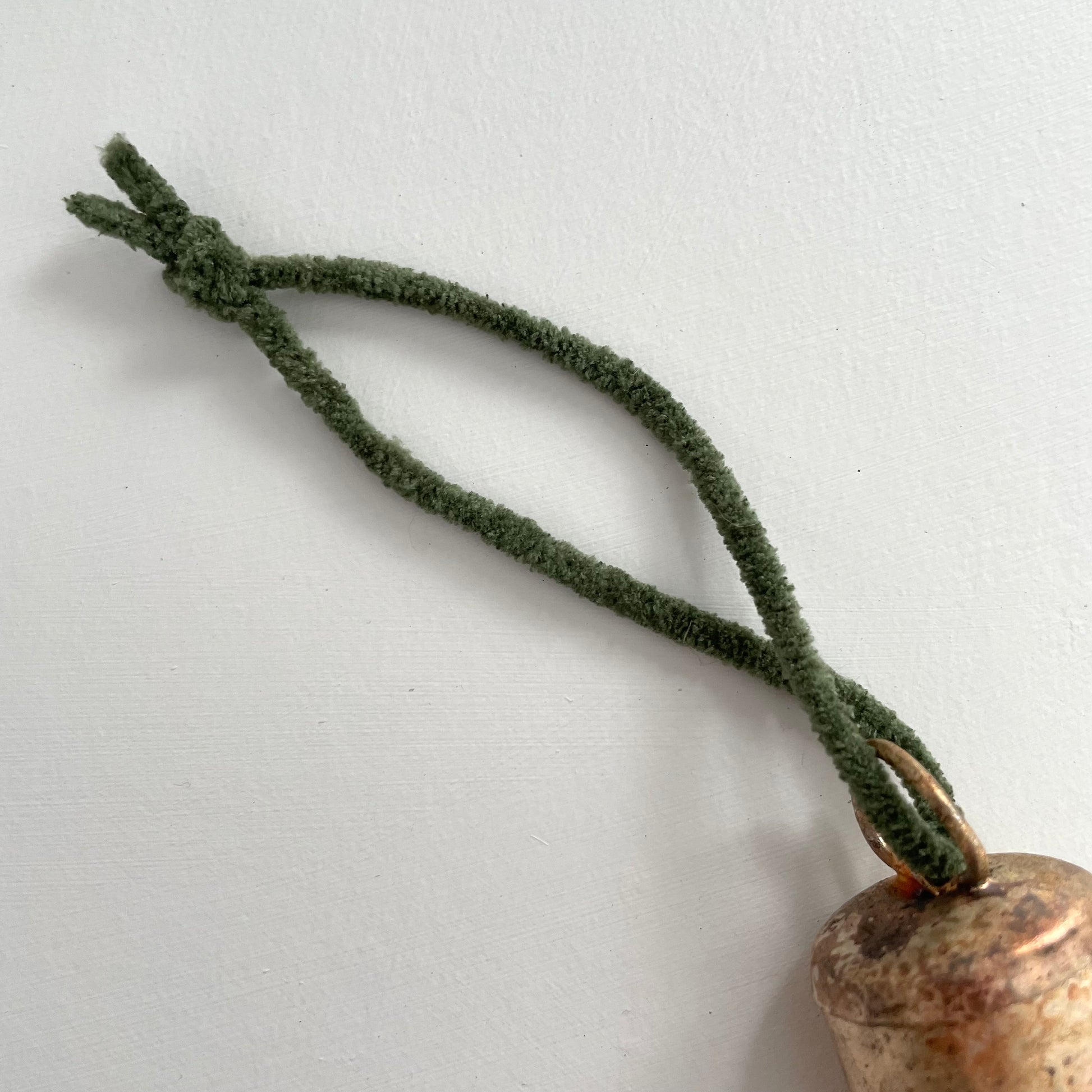 1 3/4 inch flat top tin bell with brass finish strung on twine suede and jute to make an ornament with hunter green suede cord
