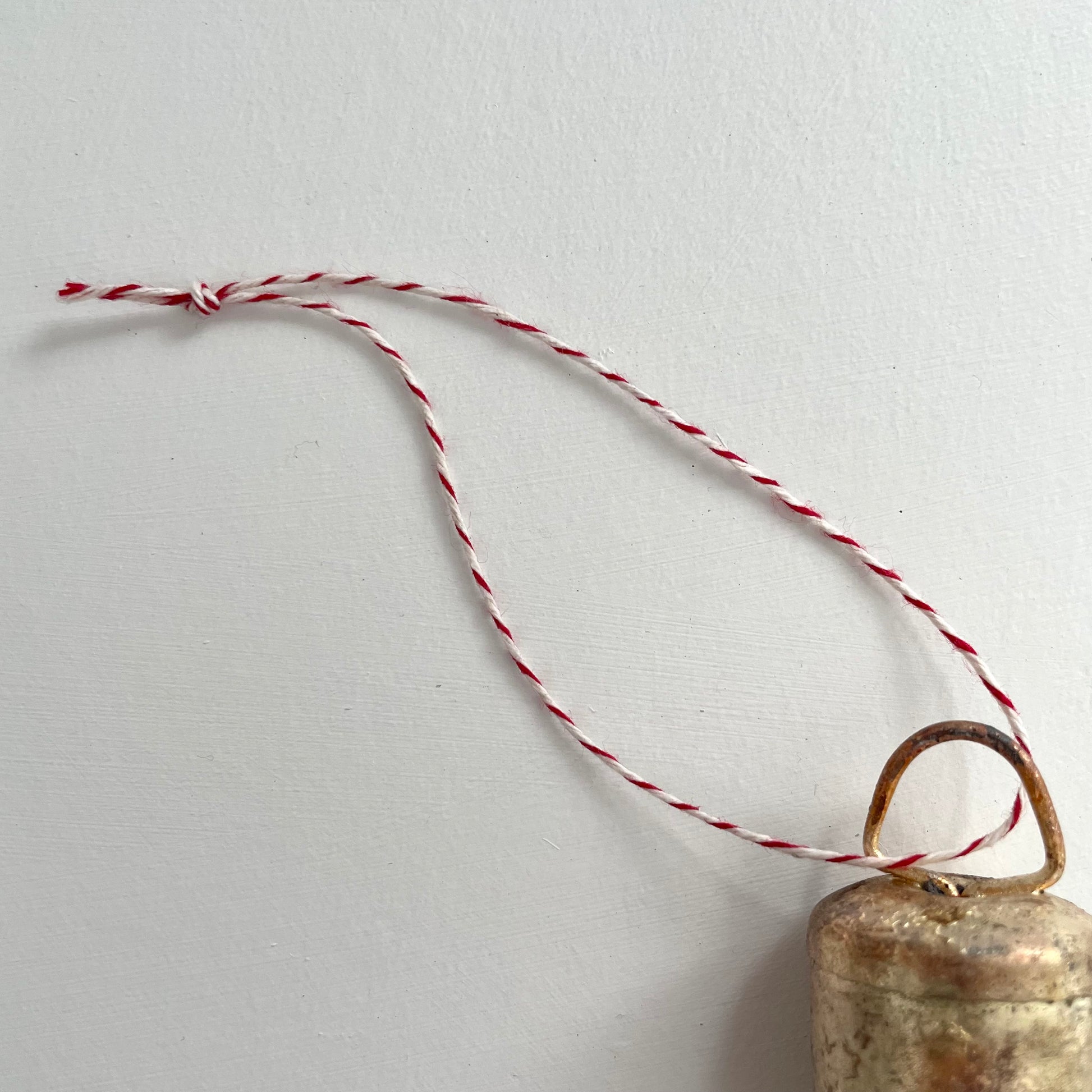 1 3/4 inch flat top tin bell with brass finish strung on twine suede and jute to make an ornament with red and white striped twine