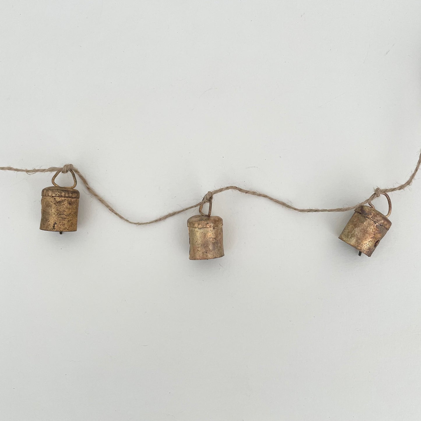 rustic flat top shaped tin bells with brass finish strung on jute for a handmade Christmas garland