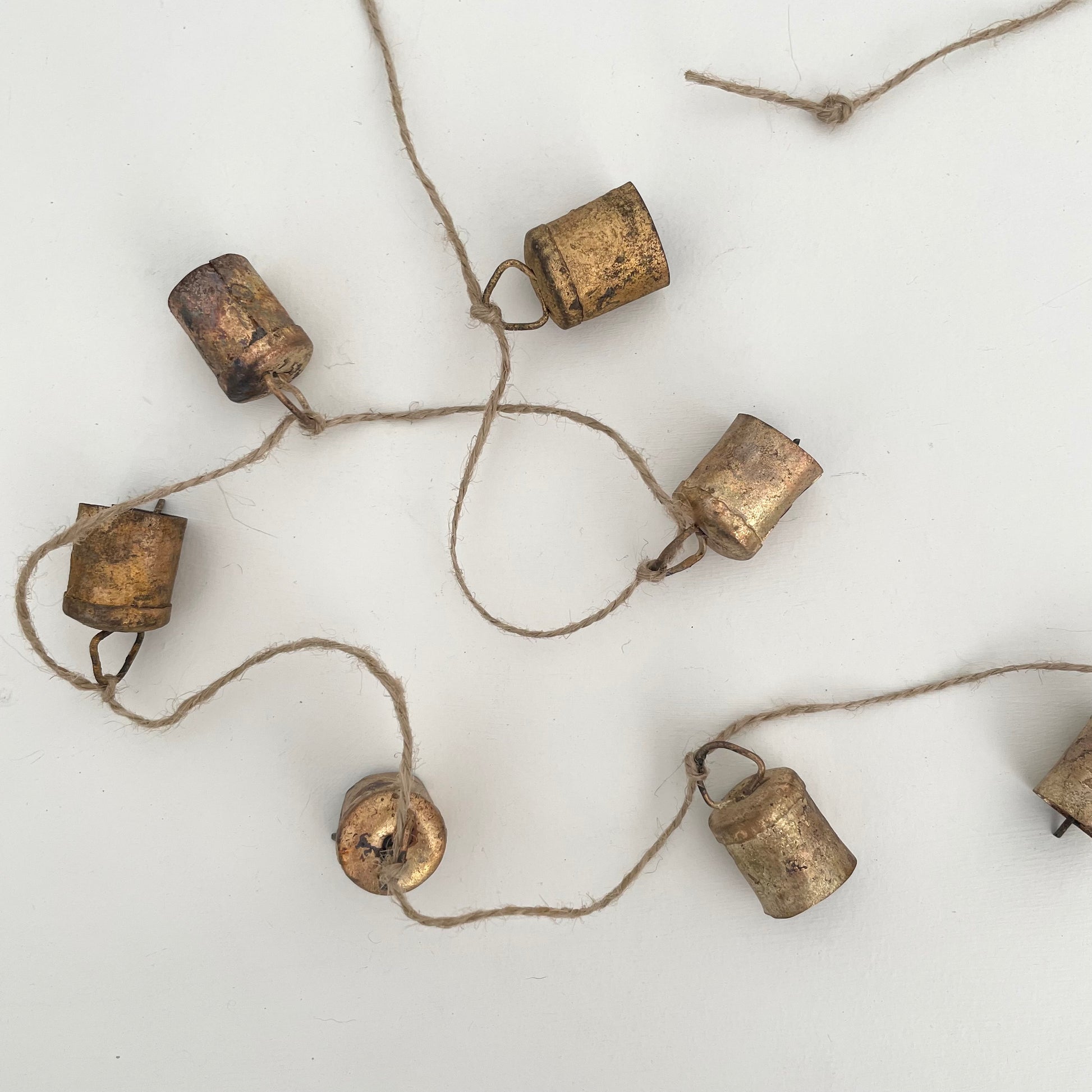 rustic flat top shaped tin bells with brass finish strung on jute for a handmade Christmas garland