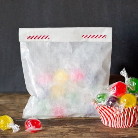 translucent white glassine bags in two sizes holding treats with a red and white striped twist tie closing the bag and a cupcake liner holding treats next to it