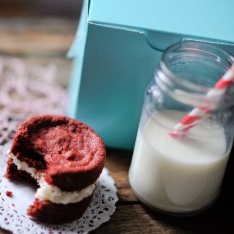 turquoise 4x4 square bakery box next to a stack of whoopie pies and bottle filled with milk