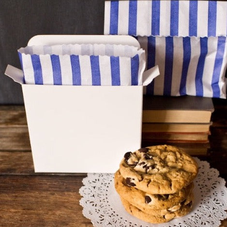 individual solid white cardboard cookie box next to a stack of chocolate chip cookies
